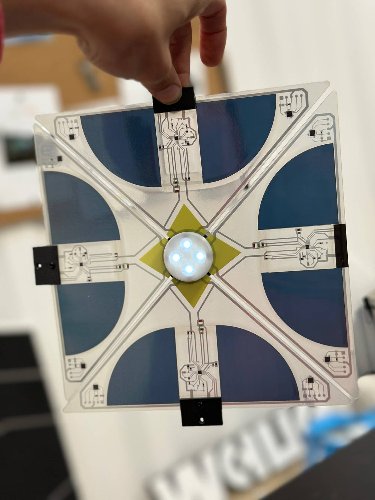 Hand holding a translucent Between Lights prototype with printed circuits, flexible solar cells and four illuminated LEDs