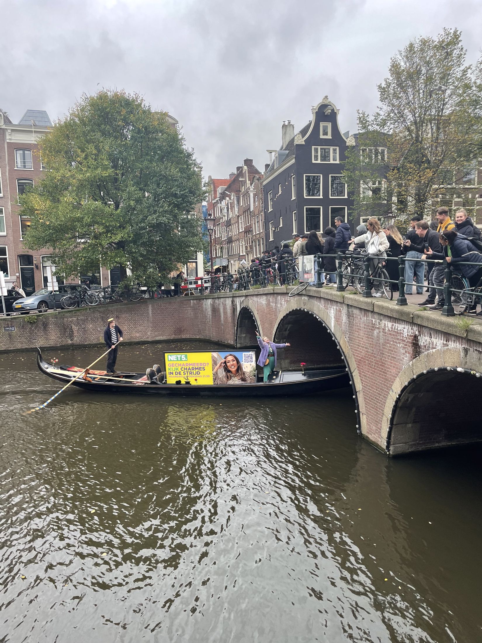 Net5-branded gondola passing an arched Amsterdam bridge while a crowd watches