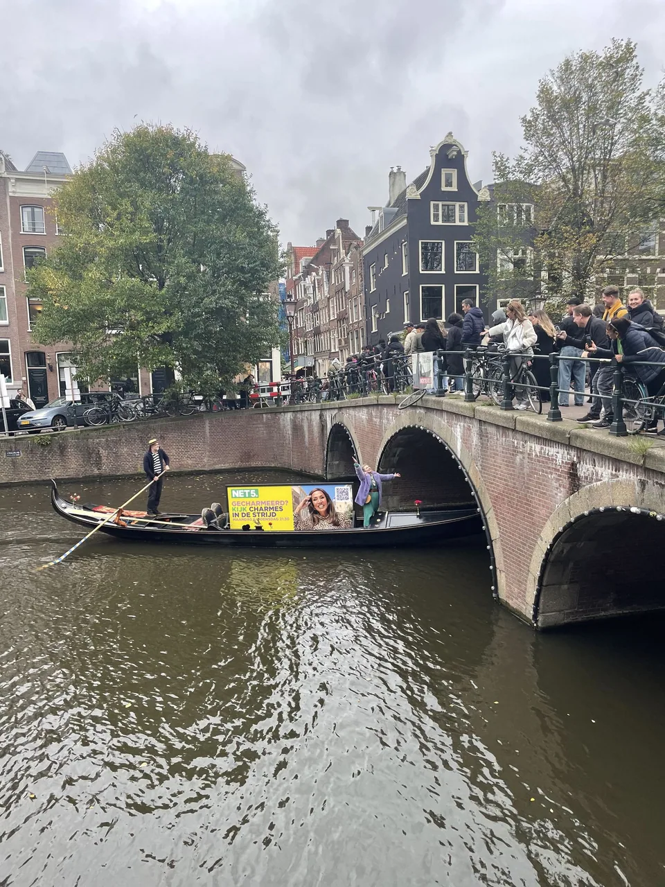 Net5-branded gondola passing an arched Amsterdam bridge while a crowd watches